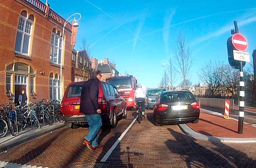 In de Hobbemastraat wordt wegens werkzaamheden de rijbaan geblokkeerd. Ouders die kinderen naar het Zuiderbad brengen parkeren hun auto schaamteloos over de gehele breedte van de weg.